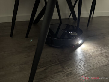 Il Roborock Qrevo Slim con la sua luce accesa nel labirinto di gambe della sedia